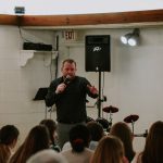 A man performs stand-up comedy in front of an audience in a small venue.